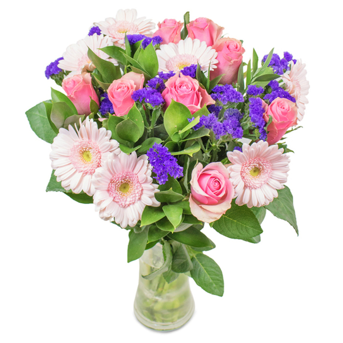 A striking floral arrangement stands poised in a slender, clear glass vase, set against a crisp white backdrop-a vision of elegance from Clapham's local flower scene. The bouquet features approximately seven to nine mid-pink roses, many tightly furled or with petals just starting to spiral open, displaying the classic romance that roses have long symbolised near Clapham Old Town. Among them, about five to seven pale pink gerbera daisies with large, round heads and subtly lighter centres add a contemporary softness, their blooms reminiscent of fresh spring mornings by the Common. Pops of vivid purple statice weave through the arrangement, creating dynamic contrast and texture amidst the pastel palette. The abundance of deep green foliage forms a lush, verdant base, imbuing the bouquet with a sense of both depth and freshness-evocative of leafy vistas along The Pavement or Clapham North's tree-lined streets. Visible stems nestle in clean, clear water, highlighting the freshness of every flower and reinforcing the natural, just-picked feel of a same-day delivery from a trusted Clapham florist. This arrangement, with its romantic pink hues and sprightly purples, feels equally at home as a birthday surprise, a Mother's Day tribute, or a simple yet meaningful gesture of affection to brighten any local residence or office.