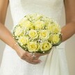 Nestled gently in the hands of a bride, this bouquet feels like a slice of morning sunshine on a peaceful Clapham lane. Pale yellow roses, their petals unfurling with soft luminosity, are gathered into a generous, rounded clutch that glows warmly against the creamy, textured fabric of the bridal dress. Tucked throughout the roses are delicate tufts of baby's breath-tiny white blooms that appear as gentle whispers of purity and hope, each adding an ethereal touch reminiscent of light drifting through the trees on Clapham Common. The base is framed by looping, verdant greenery-perhaps grass blades or scrolls of hidden wire-offering elegant support and hinting at the artistry unique to local Clapham florists. The bride's hands, flawless with a soft manicure and adorned with a single ring, cradle the bouquet in a gesture filled with anticipation and serenity. The background softly fades, ensuring all attention remains on the radiant florals and the quiet joy of the gathering. This bouquet's tender palette and harmonious design perfectly capture the spirit of a romantic South London ceremony, where every petal tells a heartfelt story of celebration, artistry, and new beginnings.